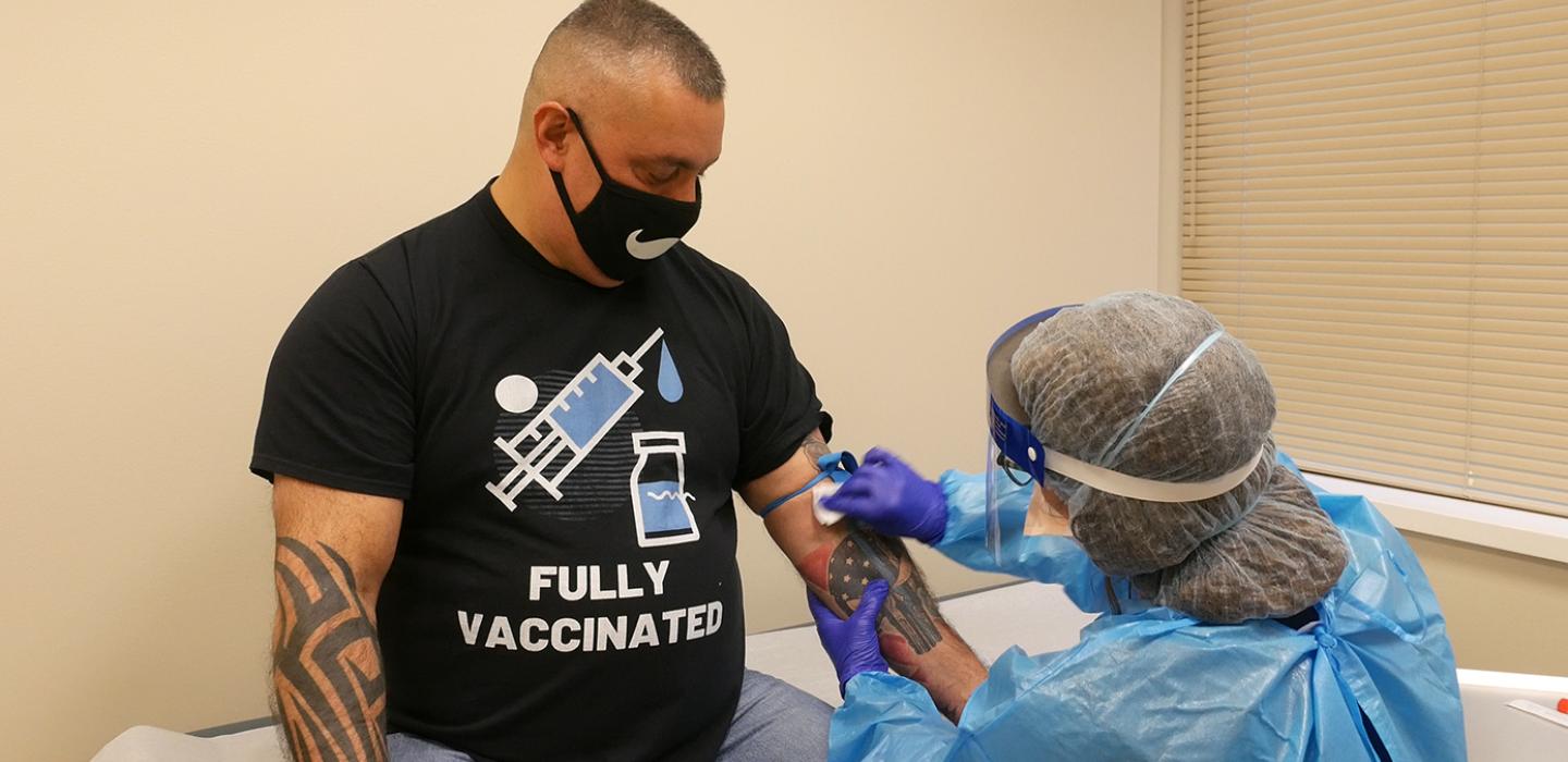 A person in a black face mask and T-shirt receiving a vaccination