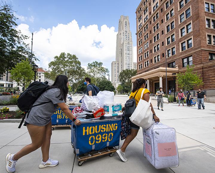 Multiple Pitt students walking with moving carts and bags