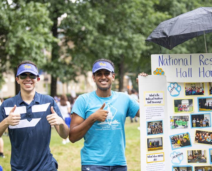 Two students smiling, holding thumbs up with sign