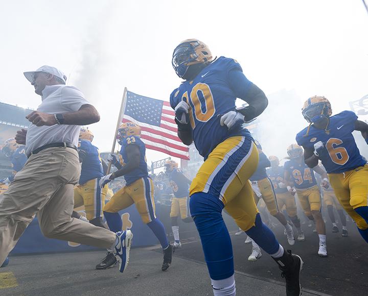 Pitt football coach running to the field with players following behind