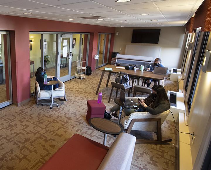 Three people studying in a study room with several tables and chairs
