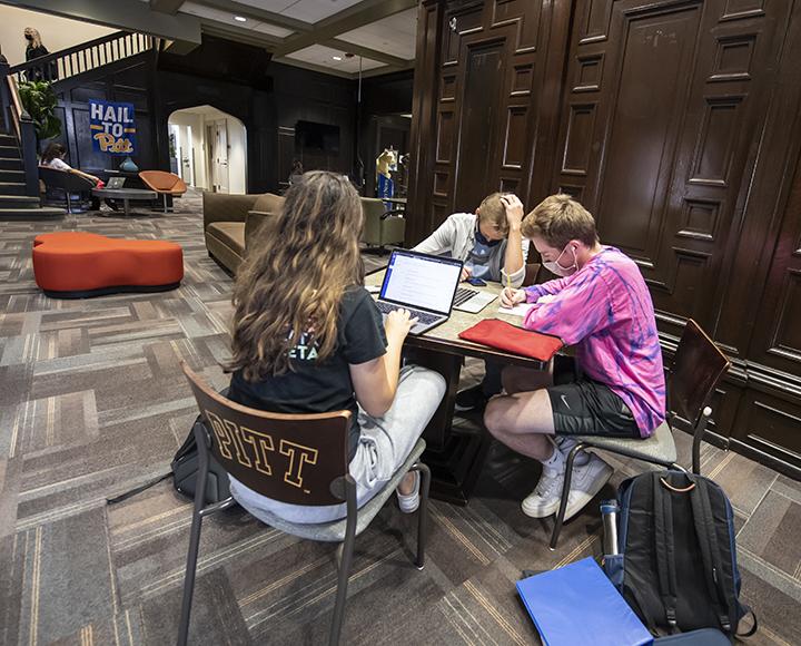 Three students studying at table together with laptops