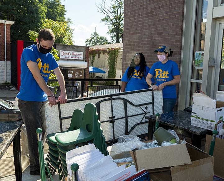 CAW volunteers with blue Pitt shirts moving tables and chairs