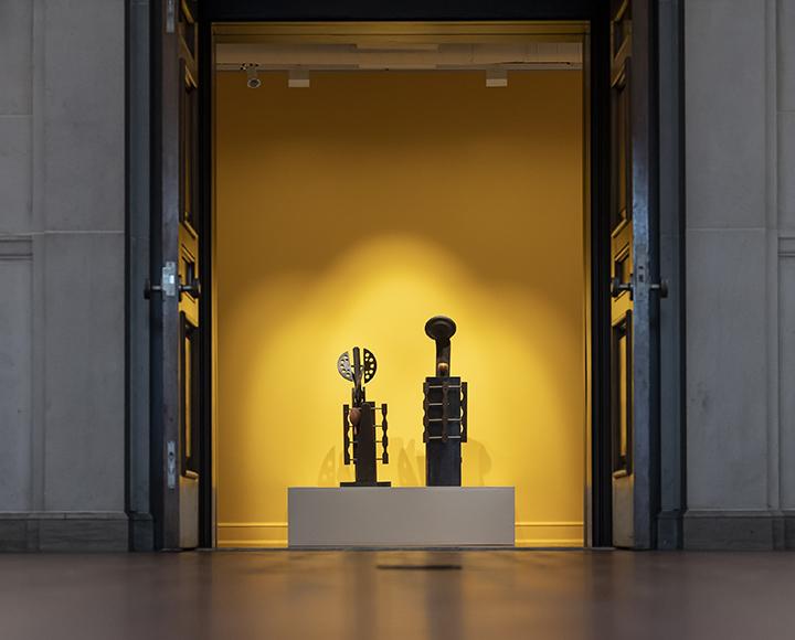 Adam and Eve sculptures displayed in front of yellow wall