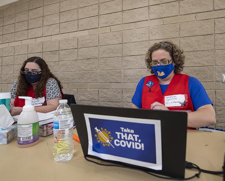 a person in a red vest in front of a laptop that says "Take that, COVID!"