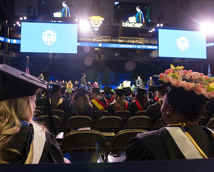 Graduating student with decorated flower cap sitting among peers during ceremony