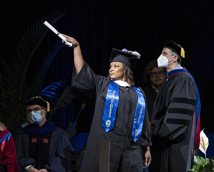 Graduating student on stage pointing diploma toward audience