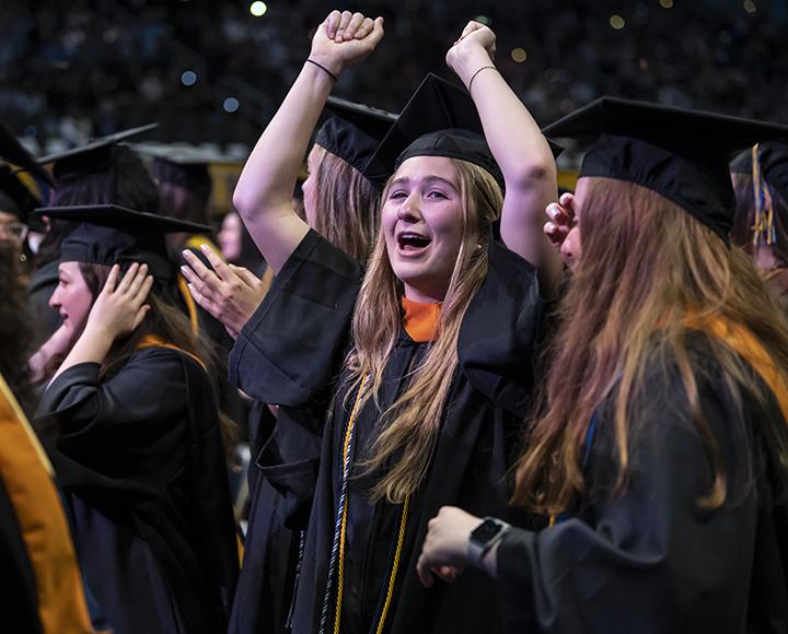 Graduating student holding arms up and cheering with peers