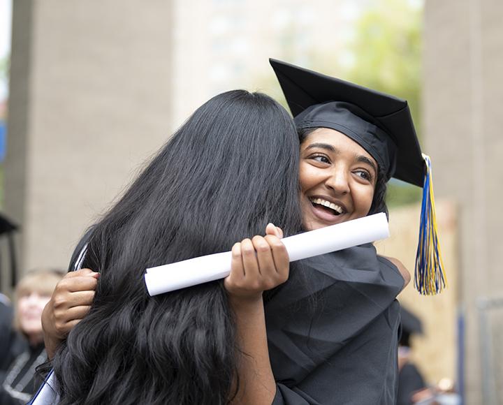 Two graduating students hugging each other with diploma in hand