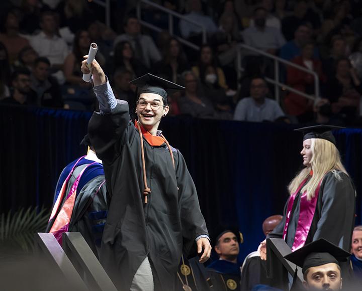Student smiling and holding diploma up high