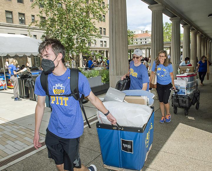 a masked student hauling a full blue bin
