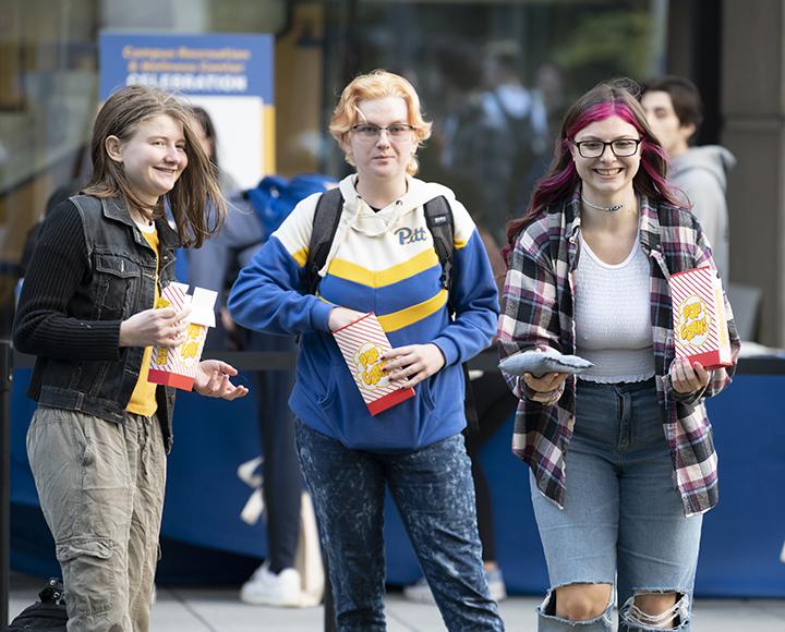 three students smiling, eating popcorn and tossing bean bags