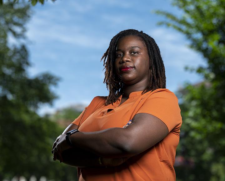 A portrait of a person in an orange shirt crossing their arms.