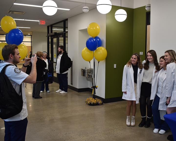 A person in a white polo photographs four people in white coats in the hallway of the new life sciences building