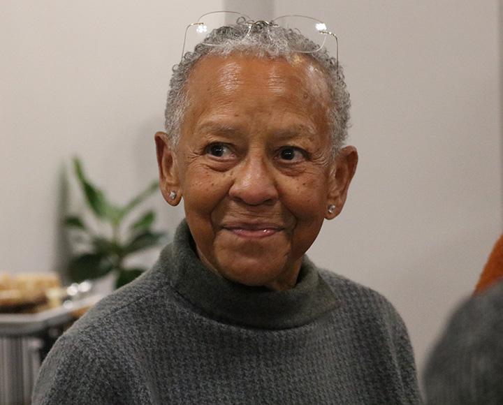 Giovanni smiles, wearing a grey sweater and glasses on her head
