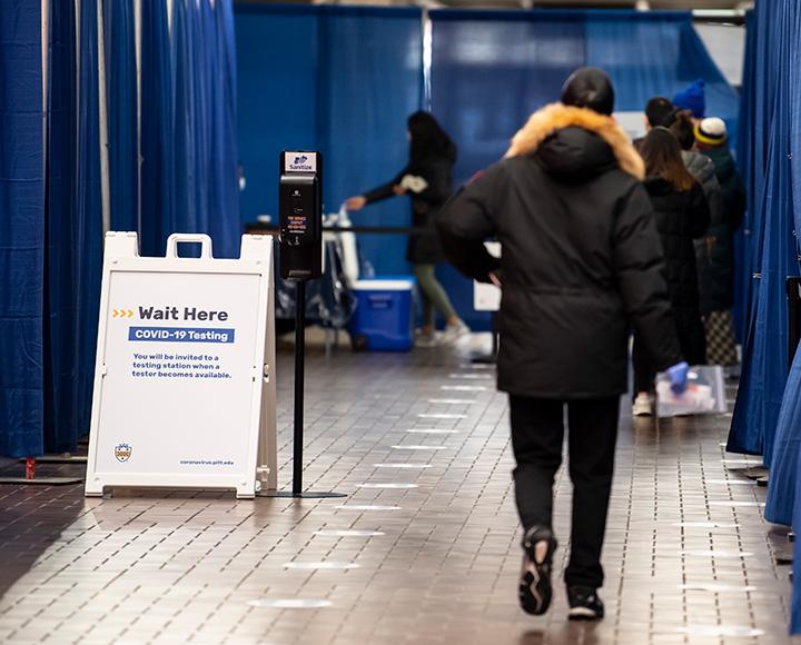 A person in a black jacket walks into a blue curtained area marked as a COVID-19 testing area
