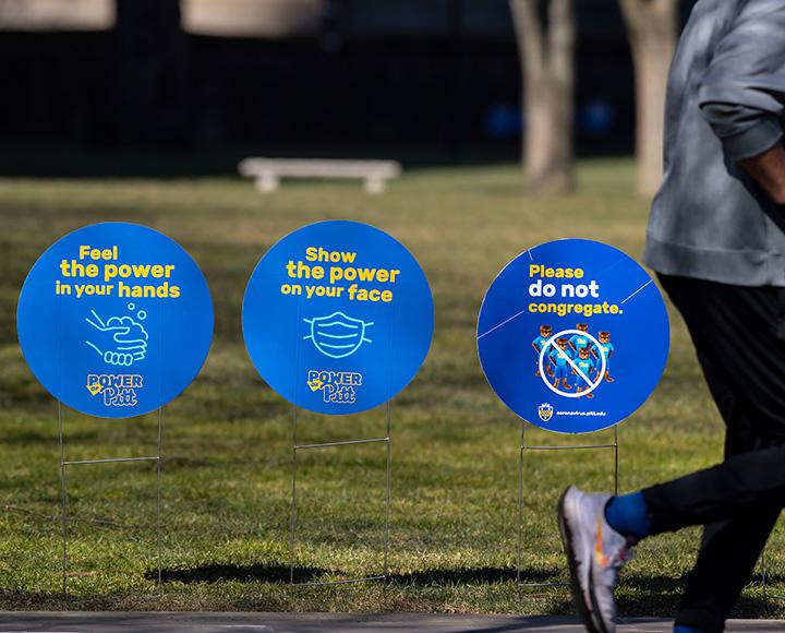 Blue circular yard signs promote mask-wearing and hand-washing
