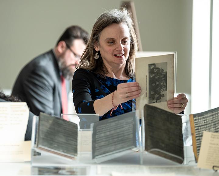 A person in a black shirt holds a sheet of paper. More archives sit on the table in front of them.