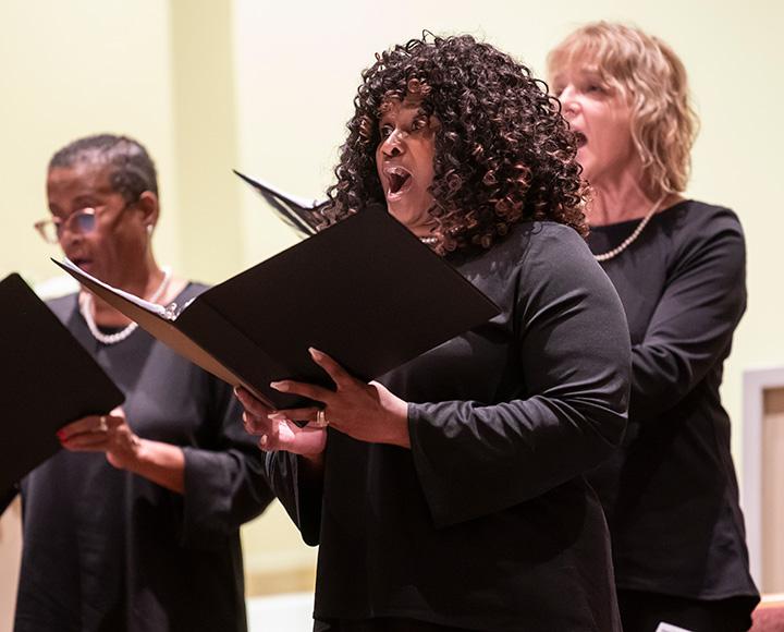 Three people wearing black sing from black folders