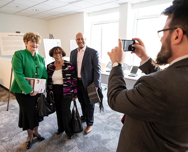 a person takes a smartphone picture of a person in a green jacket, a person in a black and pink jacket, and a person in a grey suit