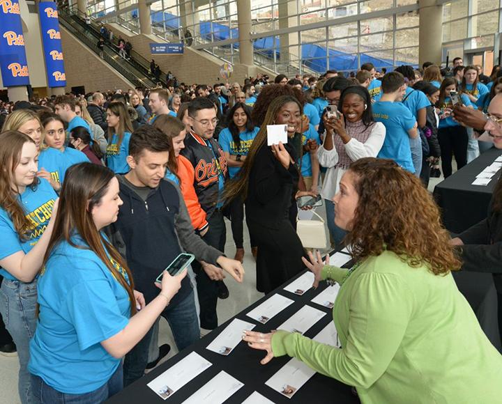 A crowd gathers around a table with white envelopes