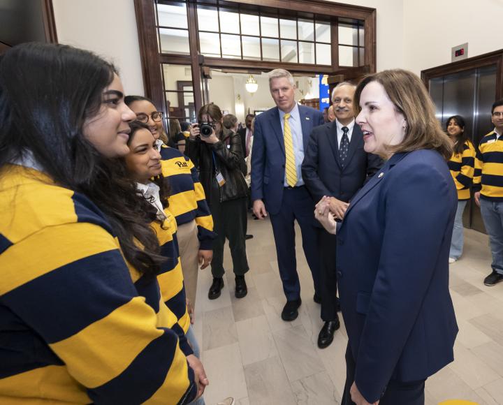 People in blue suits talk to students in yellow and blue striped polos.