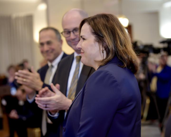 A person in a blue blazer stands as people applaud