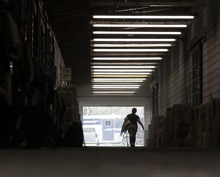 A person carries a saddle through a dark barn