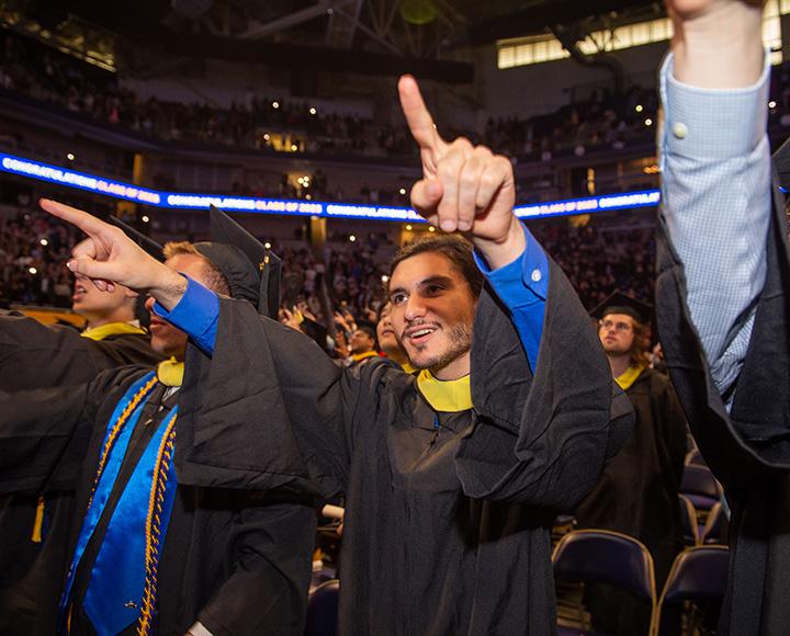 A person in graduation regalia points up