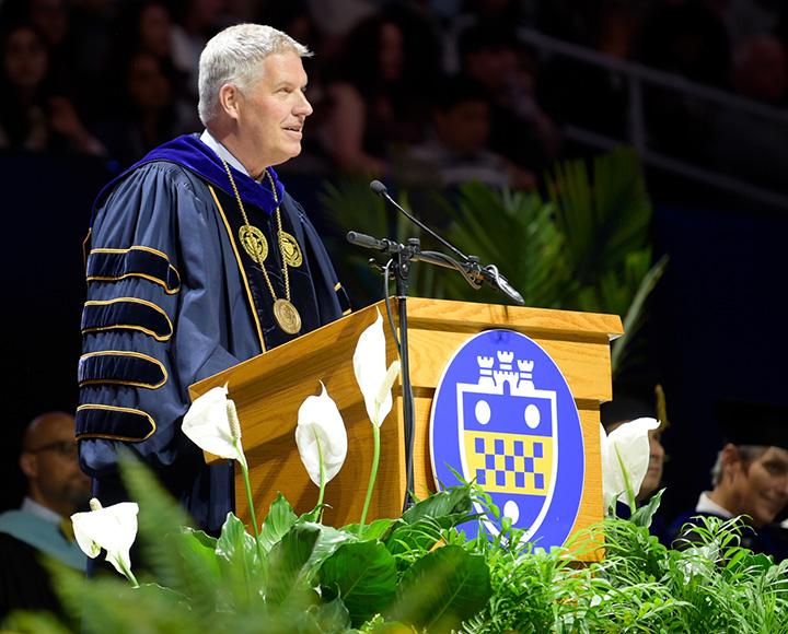 Gallagher speaks at a podium in doctorate robes