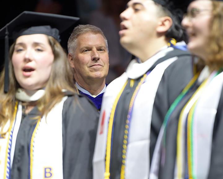 A person stands behind singing graduates