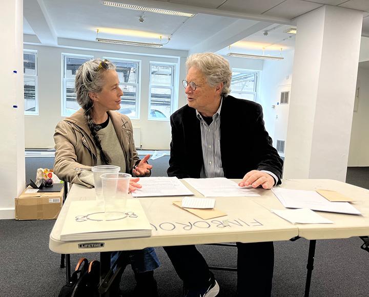 Two people talk over papers at a folding table