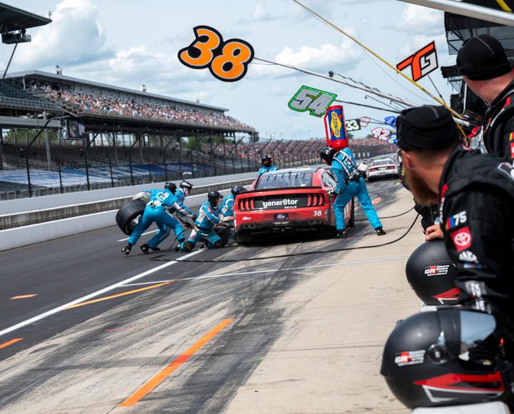 A pit crew changes a tire on a red racecar