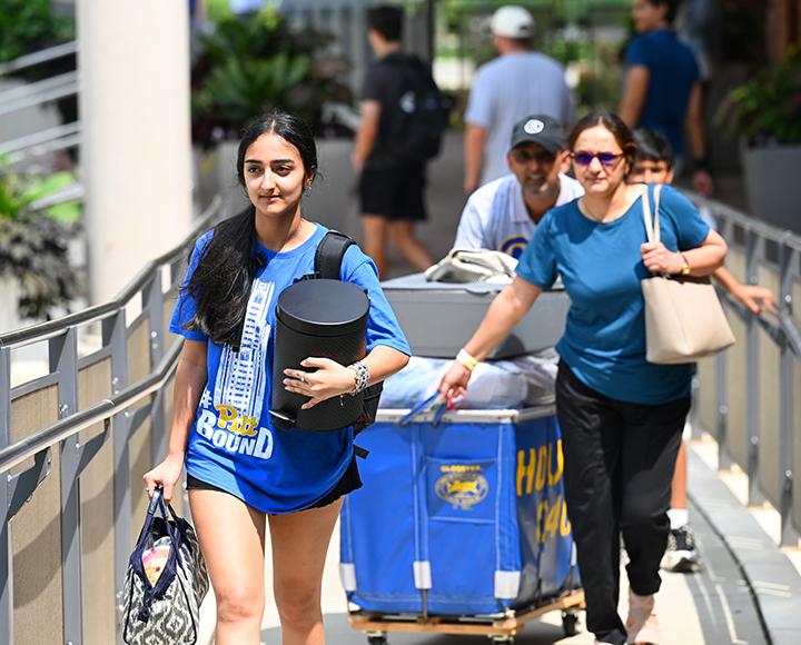 a family pushing a blue moving cart and carrying items