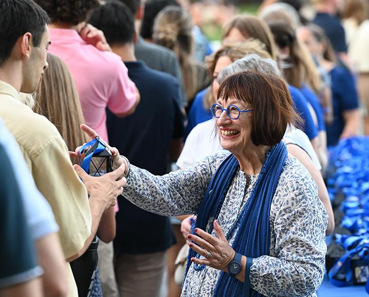 a smiling person passing on a lantern to a student in line