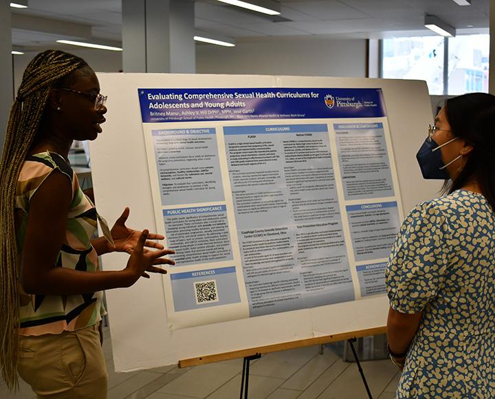 Manu explains their work to a person in front of a poster