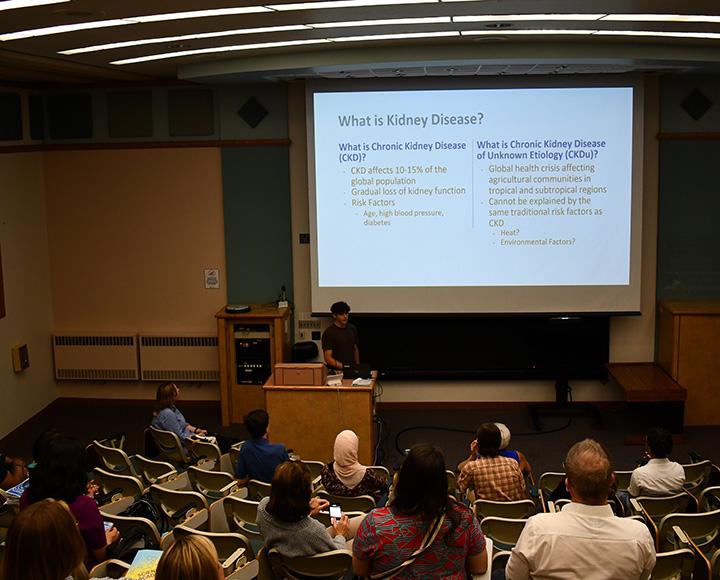 A person presents behind a podium at the front of a classroom