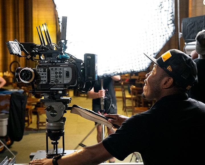 A person adjusts a video camera on a tripod