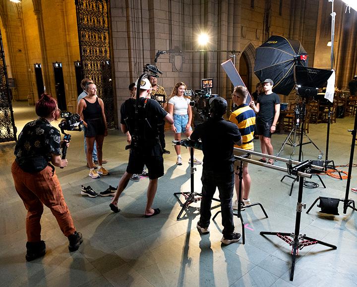 A film crew stands around a group of people inside the Cathedral of Learning