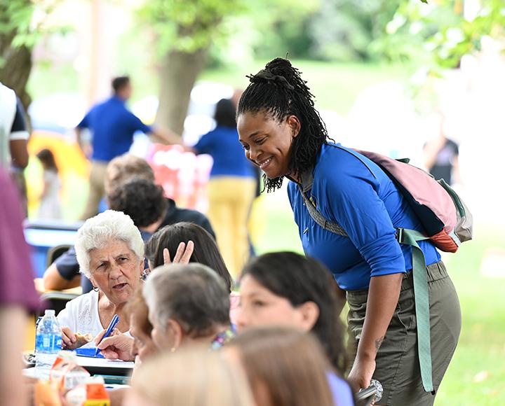 A person leans over to talk to people eating at a picnic table