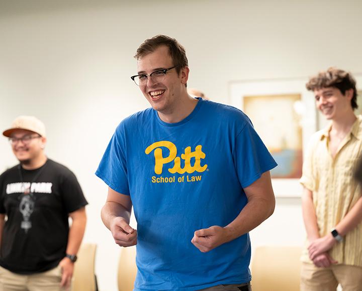 A person in a blue Pitt School of Law T-shirt laughs