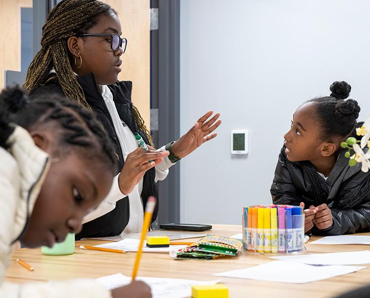 A person talks to a young student at a crafting table