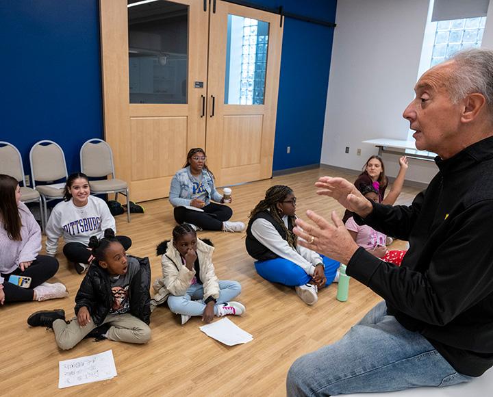 A person sitting in a chair addresses people sitting on the floor