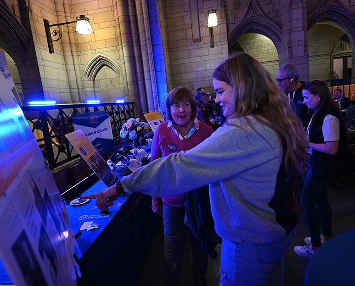 A girl points at another person's informational poster on a table