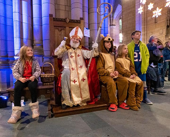 Children in pajamas sit next to St. Nicolas