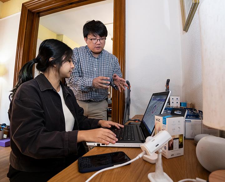 A professor gestures to a student working on a laptop