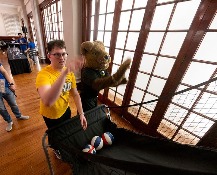 A person and a panther mascot shoot basketballs at a net game