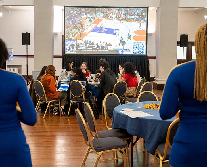 People sit at a table in front of a projector playing a basketball game