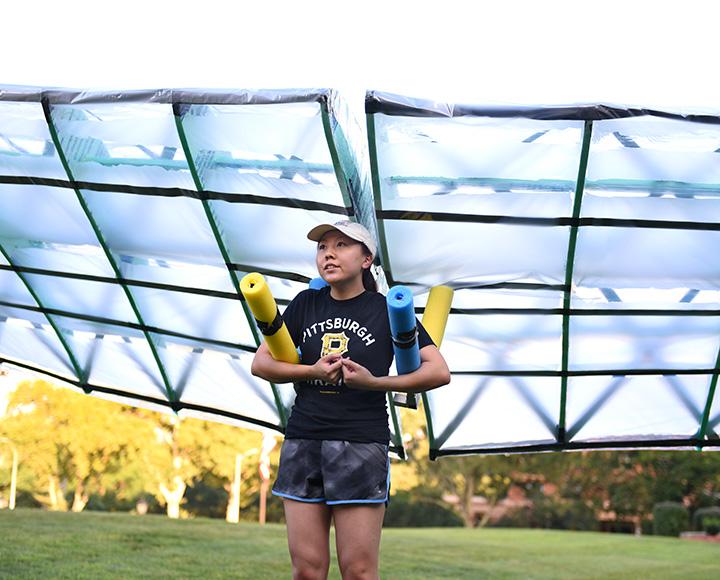A person stands in a field with a plastic glider on their back