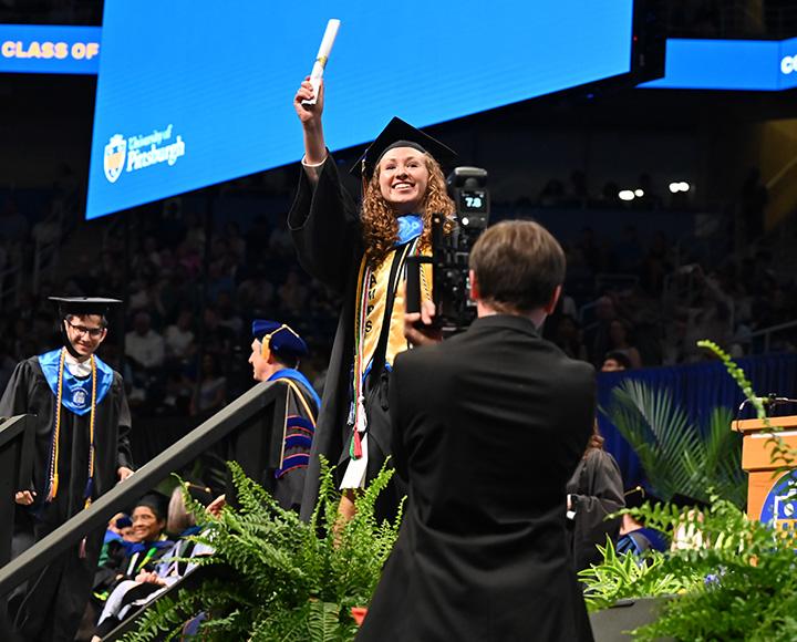 A graduate holds their diploma aloft as they exit the stage